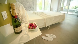 Habitación de hotel con una cama, una botella de champán, un tazón de fresas y un par de pantuflas en el suelo.