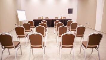 Un salón de conferencias con filas de sillas frente a una larga mesa, una pizarra y un televisor de pantalla plana en la pared.