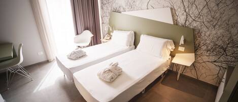 A hotel room with two beds, a desk, a chair, and a large window with curtains.