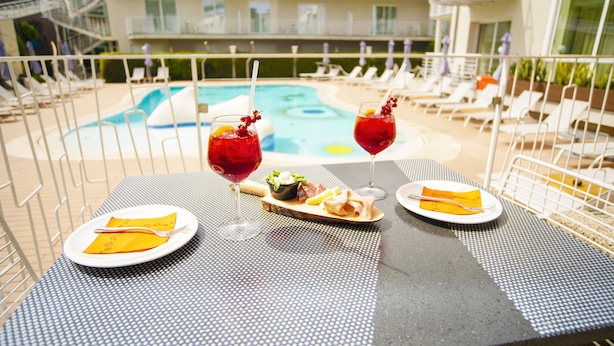 Una mesa con comida y bebidas, con vista a un área de piscina con sillas de descanso y un edificio al fondo.