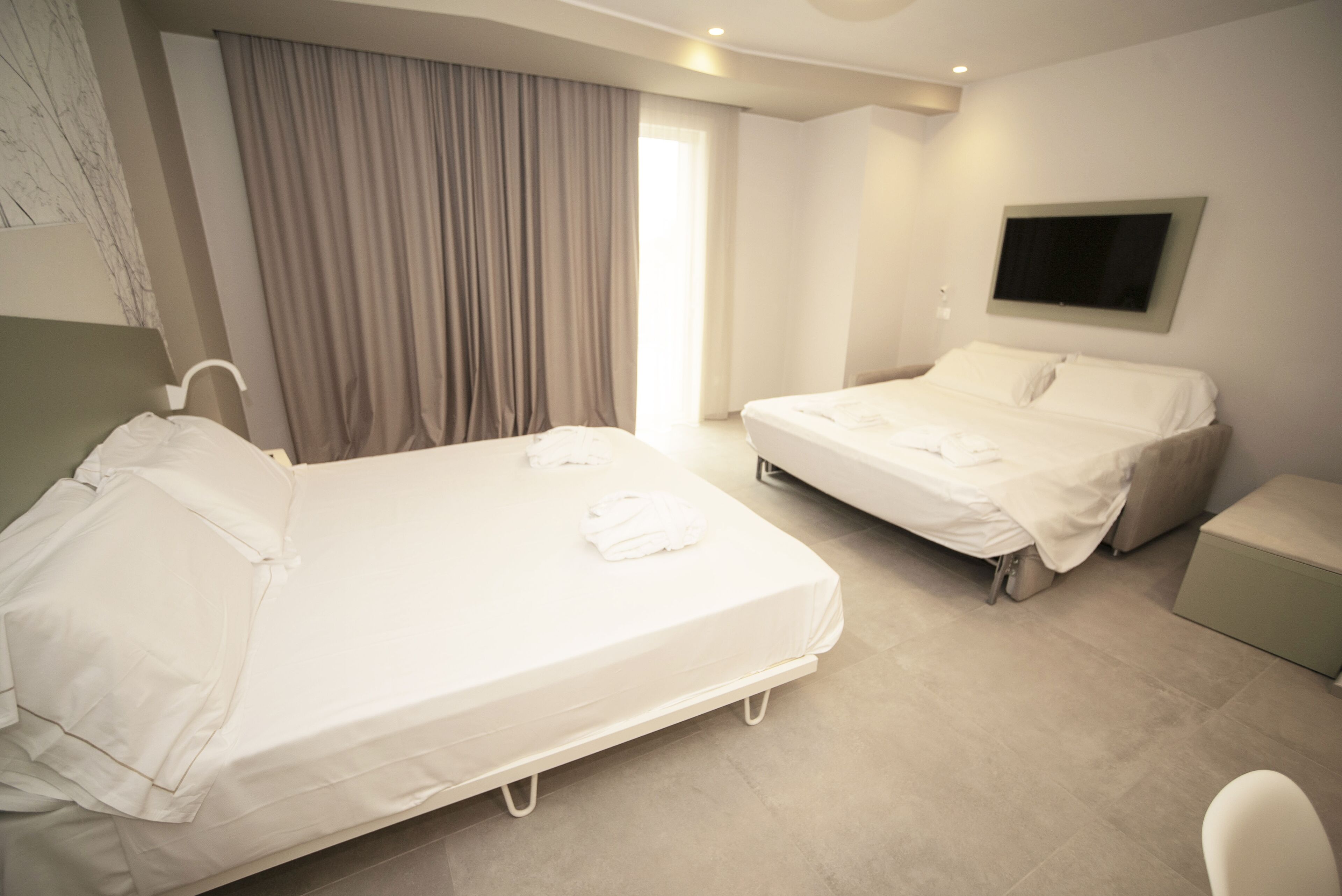 A hotel room with two beds, a TV mounted on the wall, and a window with curtains.