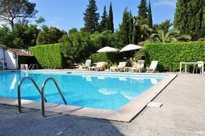 Ein rechteckiger Swimmingpool mit einer Metallleiter an einer Seite, umgeben von weißen Liegestühlen und Sonnenschirmen.