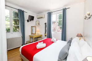 Ein Hotelzimmer mit Bett, Schreibtisch, Stuhl, Fernseher und einem Fenster mit Vorhängen.
