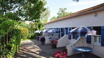 A building with a white exterior and blue accents, featuring outdoor seating with umbrellas and potted plants.