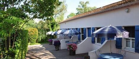 A building with a white exterior and blue accents, featuring outdoor seating with umbrellas and potted plants.