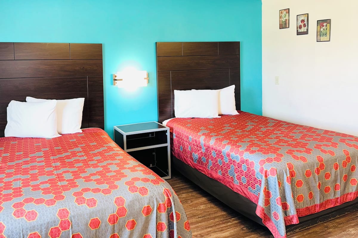 A hotel room with two beds, each with a patterned bedspread and white pillows, against turquoise walls.