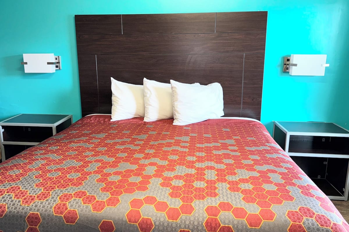 A hotel room with a large bed, a dark wooden headboard, two bedside tables, and a teal-colored wall.