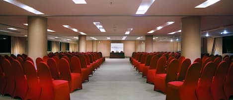 A conference room with rows of red chairs, a podium, and a projection screen.