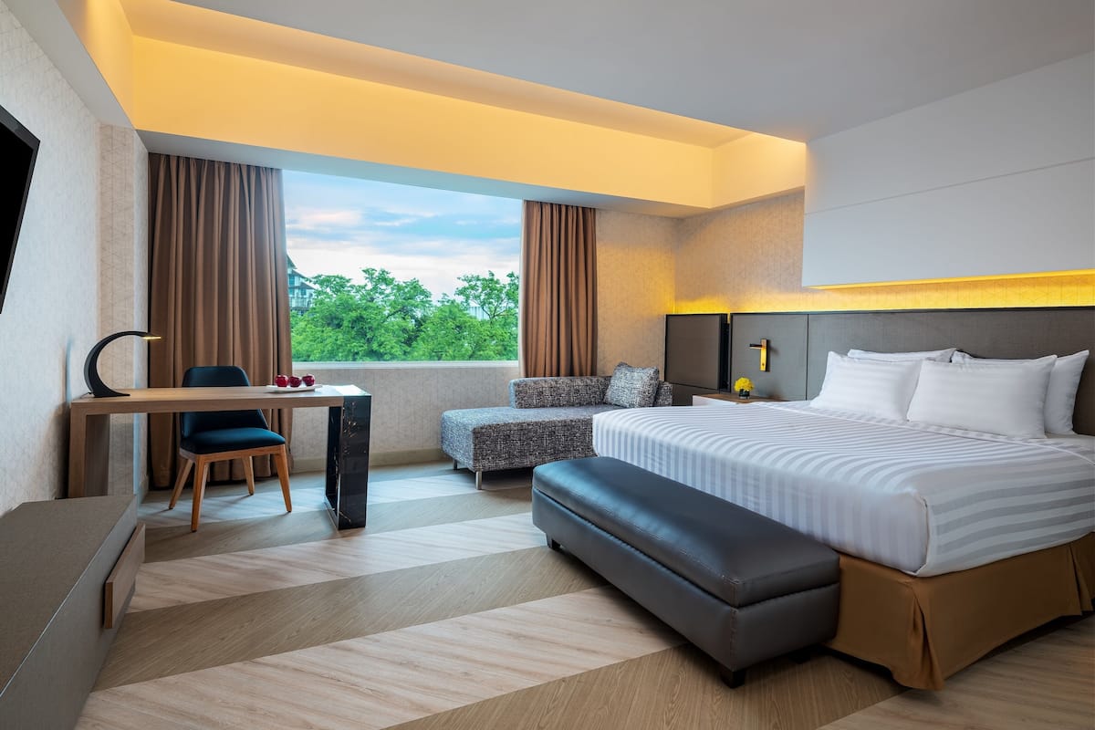 Habitación de hotel moderna con una cama grande, un escritorio con silla, un sofá y vistas a zonas verdes.