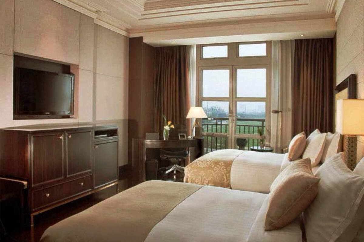 Habitación de hotel con una cama grande, un televisor montado en la pared, un escritorio con lámpara y vistas a un paisaje verde a través del ventanal.