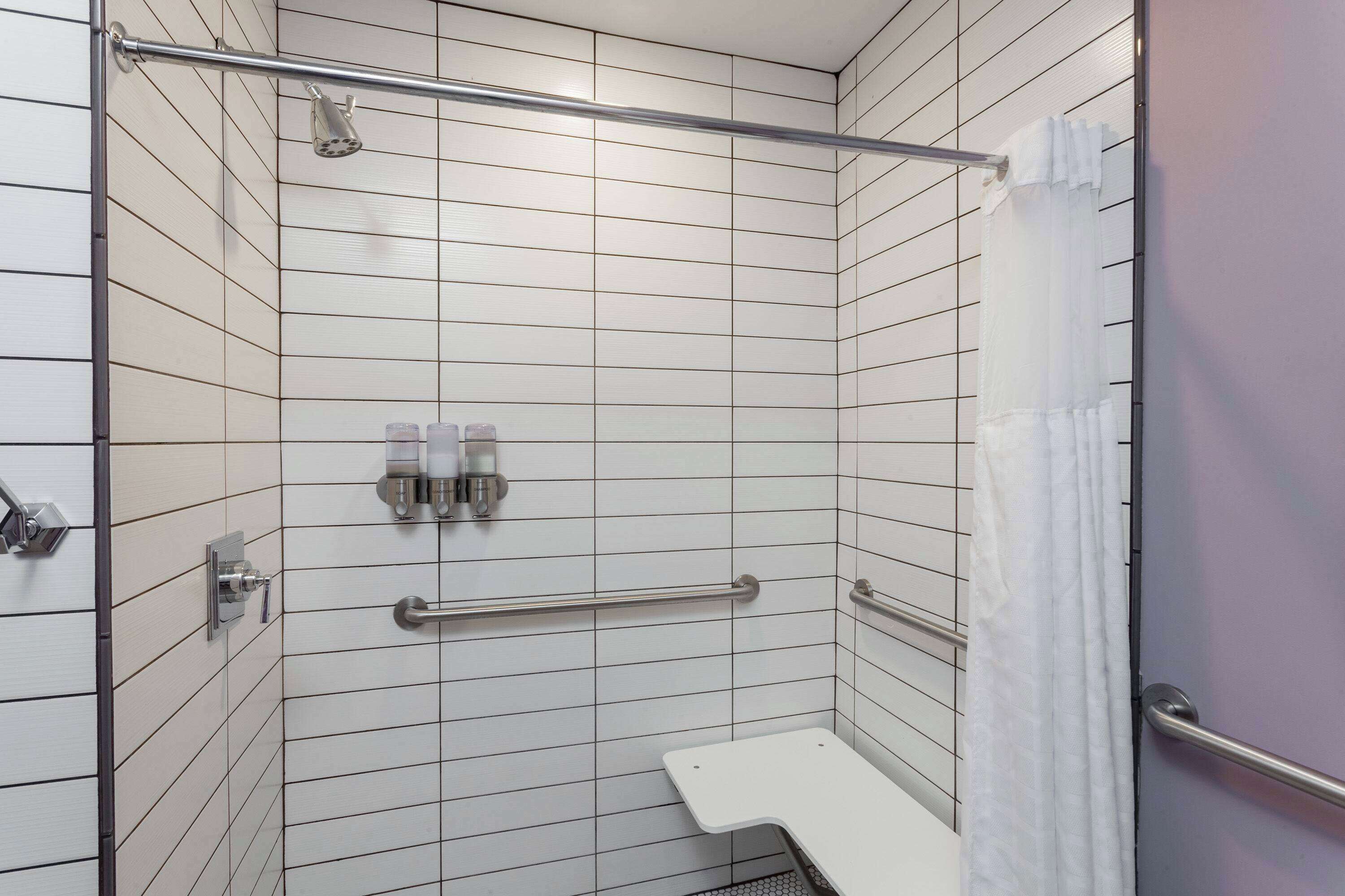A shower with white tiles, a grab bar, and a showerhead.