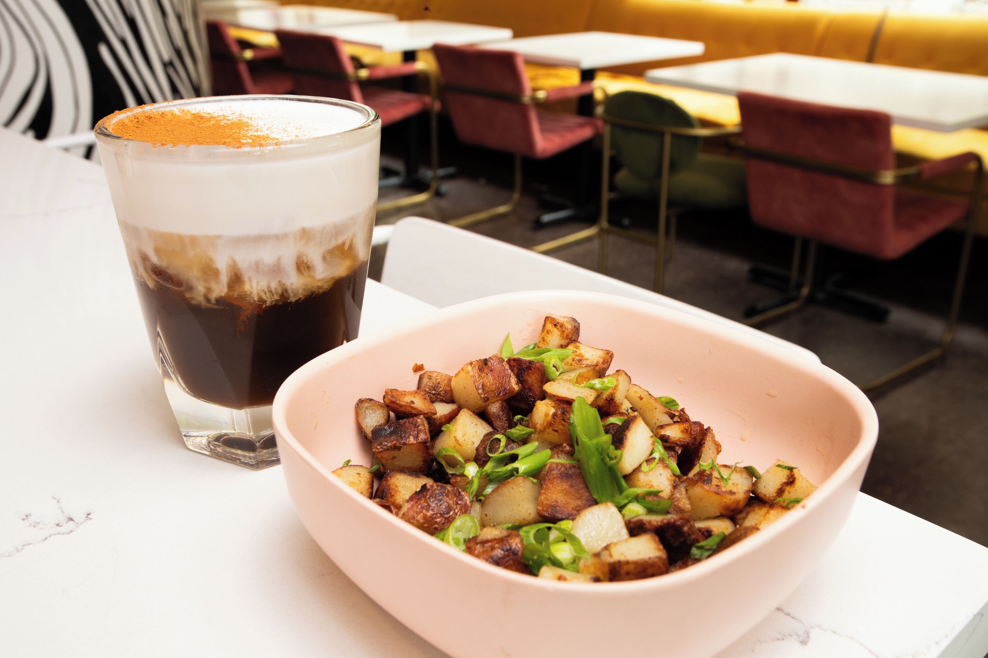 Une table à manger avec un saladier de pommes de terre rôties et un verre de café glacé.