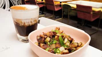 A dining table with a bowl of roasted potatoes and a glass of iced coffee.