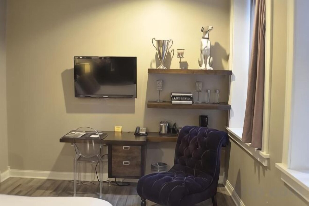 A hotel room with a bed, a desk with a chair, a television, and a window with curtains.