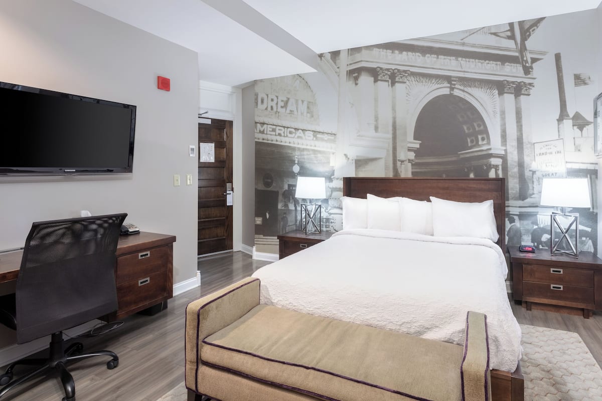 Une chambre d’hôtel avec un grand lit, un bureau avec une chaise, une télévision et une fresque murale.