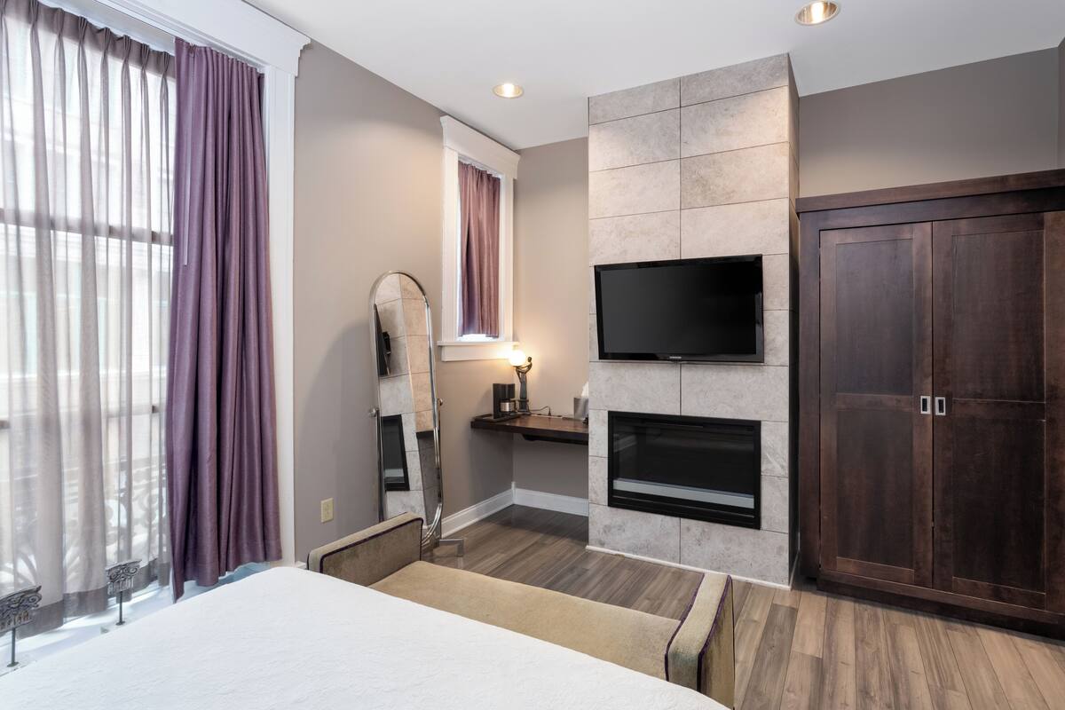 Une chambre d’hôtel équipée d’un lit, d’un téléviseur fixé au mur, d’une cheminée et d’une armoire.