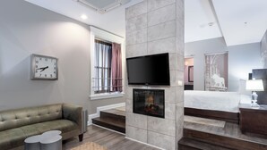 Een moderne hotelkamer met een open haard, een flatscreen televisie, een bank en een bed.