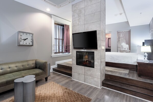 A modern hotel room with a fireplace, a flat-screen TV, a sofa, and a bed.