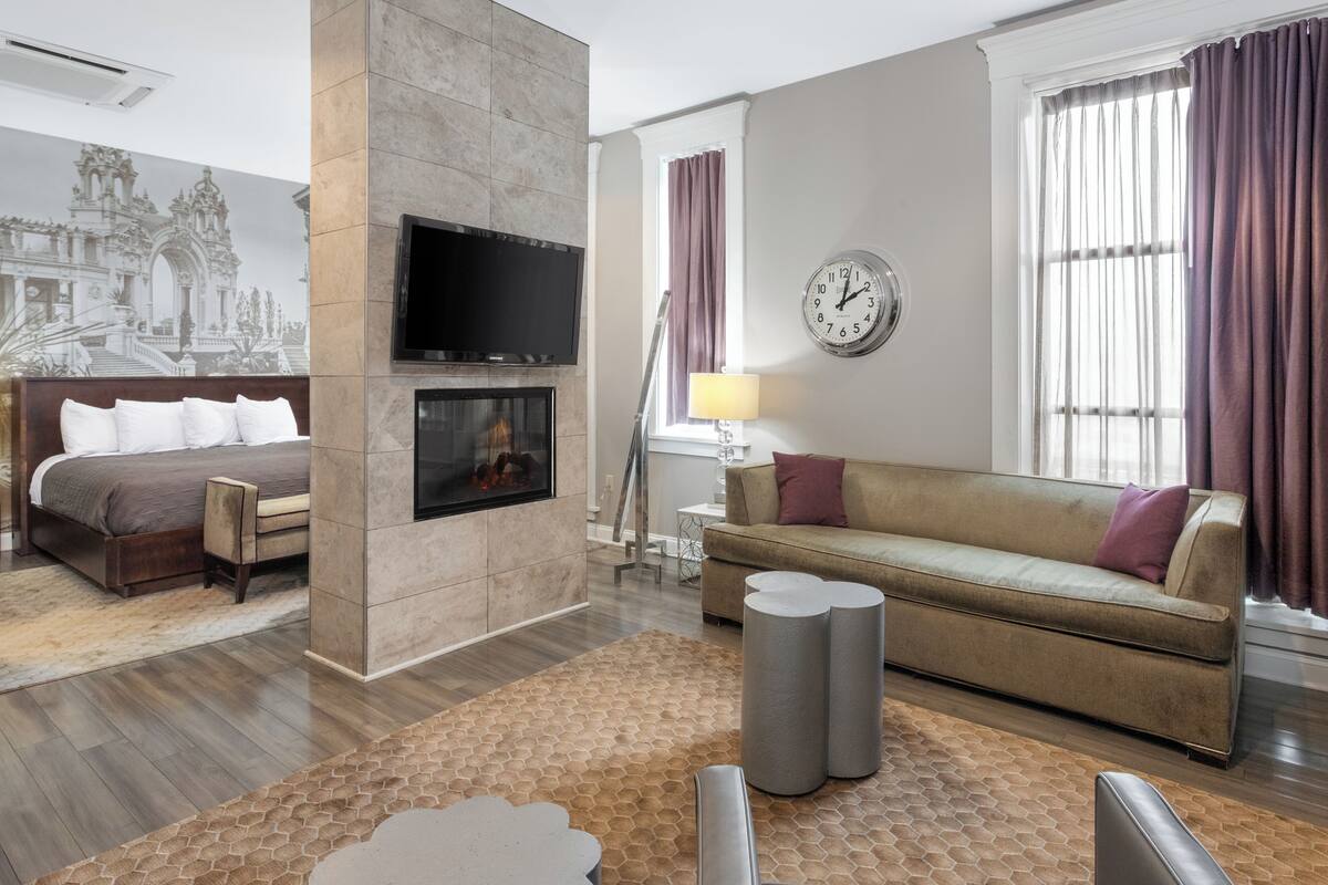 Une chambre d’hôtel moderne dotée d’un grand lit, d’un canapé, d’un téléviseur fixé au mur et d’une cheminée.