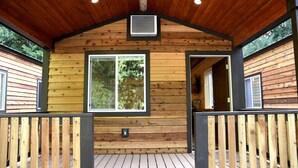 Een houten chalet met een overdekt terras, grote ramen en een centrale luchtopening.