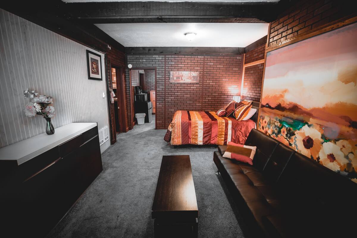 Quarto aconchegante com cama, sofá, um banco de madeira, uma mesinha e uma parede com um mural floral.
