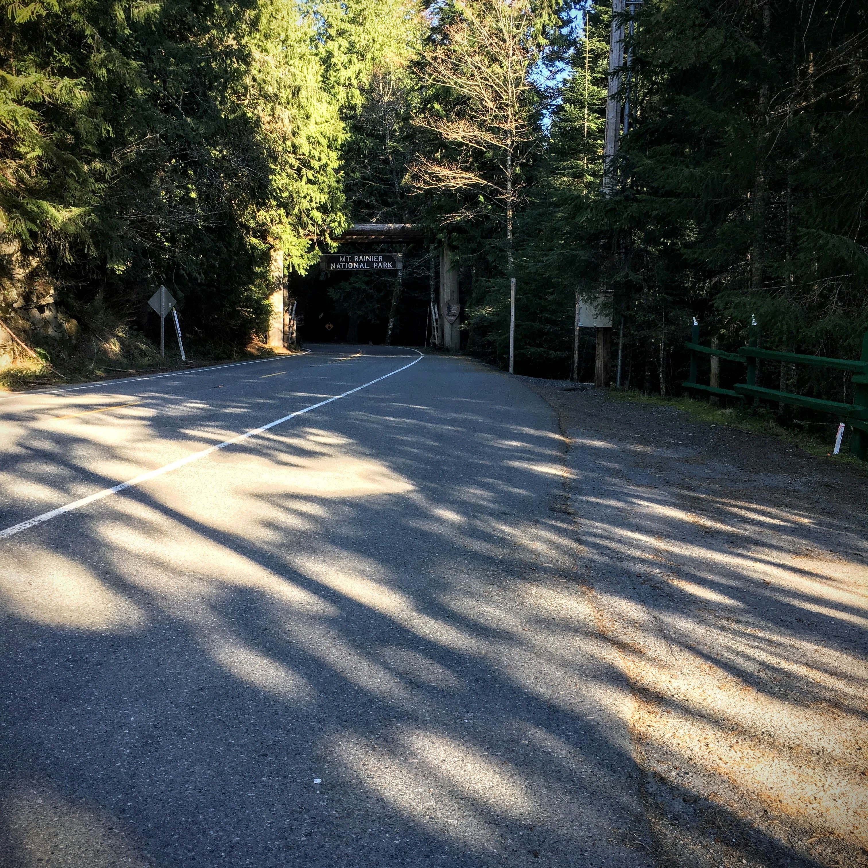 Une route menant à une zone boisée, avec un panneau indiquant le parc national du mont Rainier.