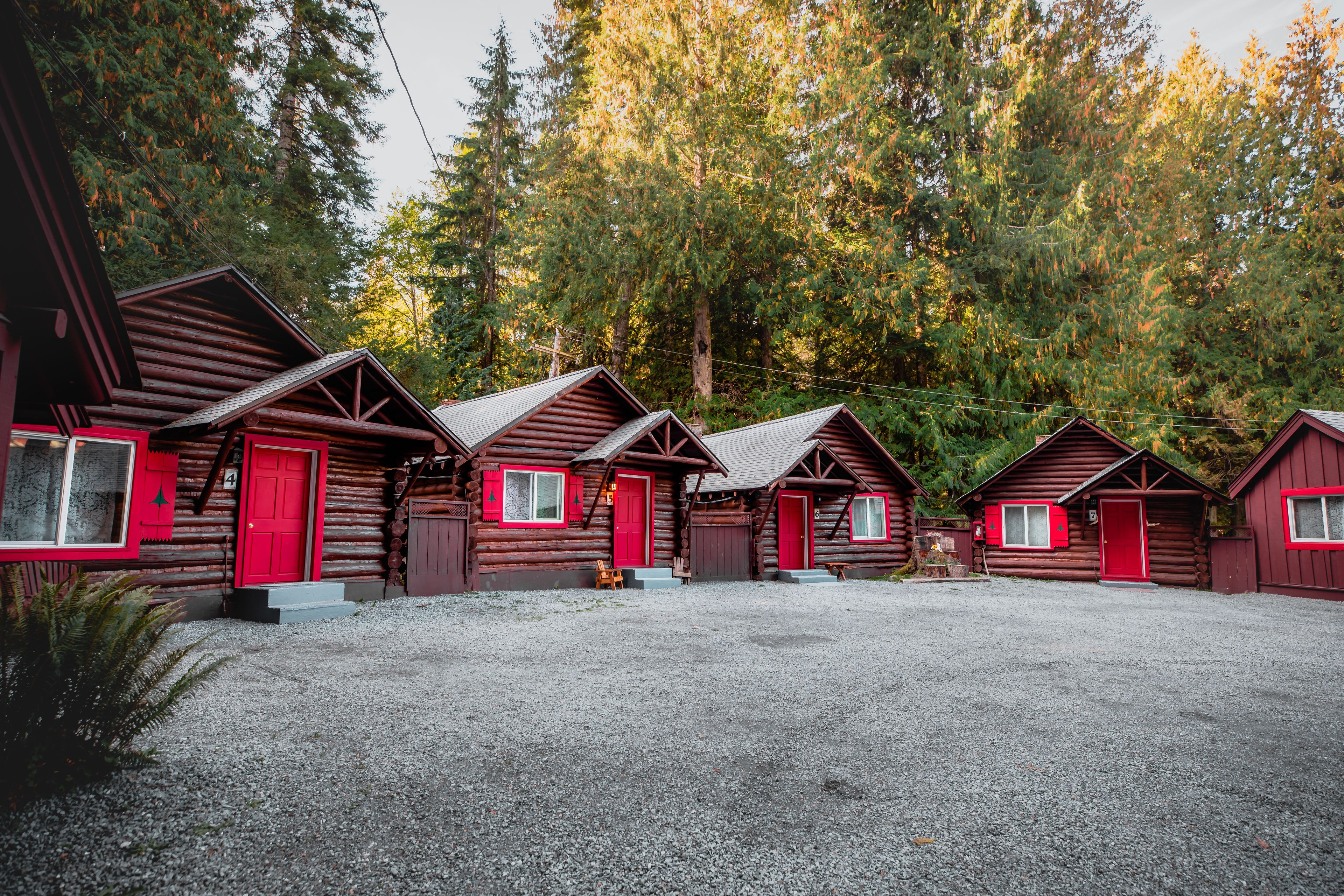 A row of log cabins with red doors and windows, surrounded by a forest.