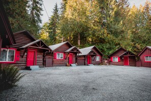 A row of log cabins with red doors and windows, surrounded by a forest.