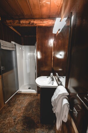 A bathroom with a wooden interior, a white sink, and a shower.