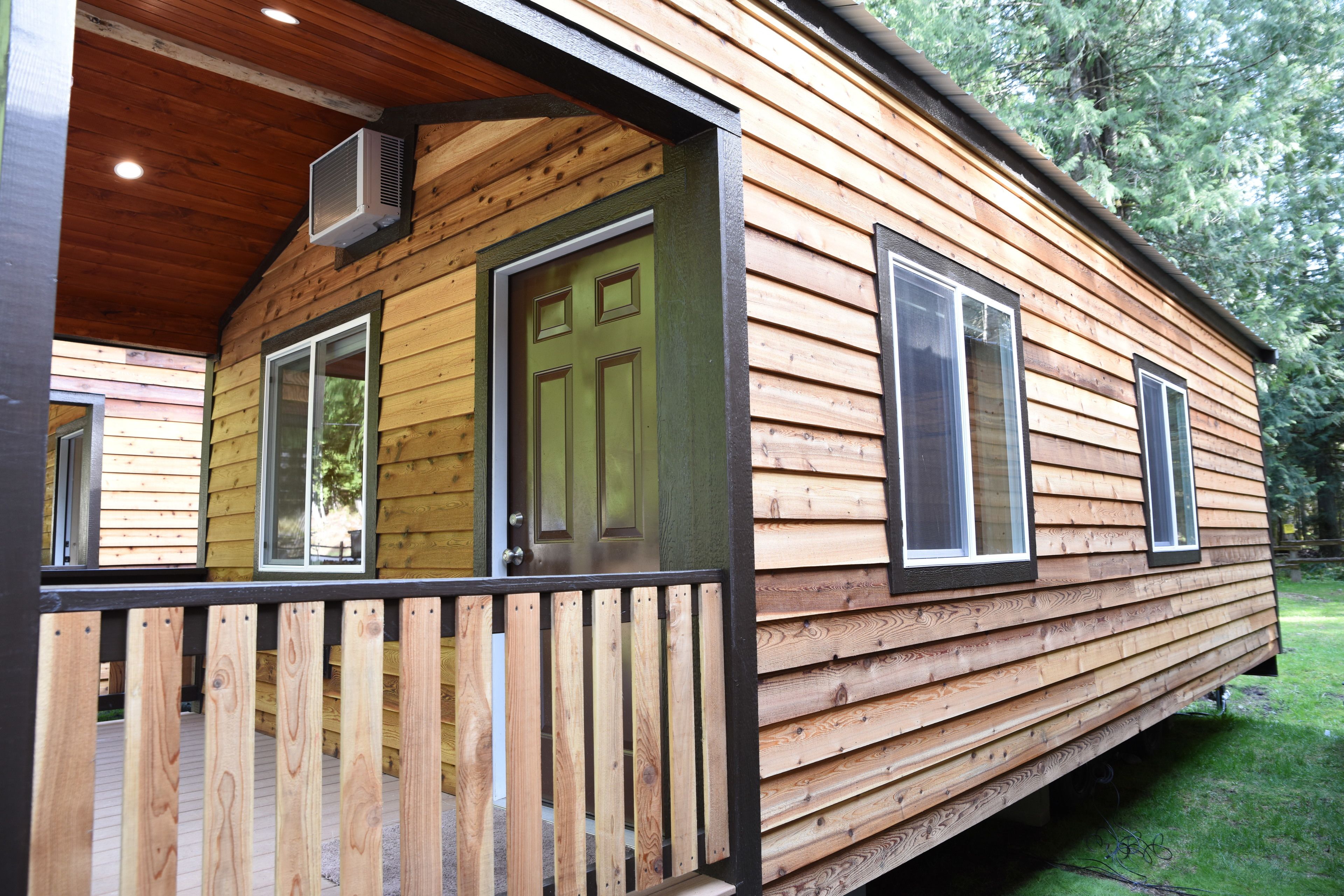 A wooden cabin with a porch, large windows, and an air conditioning unit.