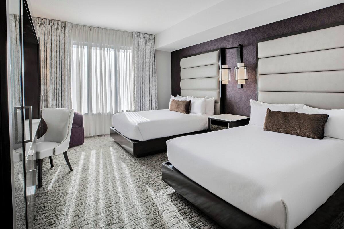 Ein Hotelzimmer mit zwei Betten, einem Schreibtisch, einem Stuhl und einem großen Fenster mit Vorhängen.