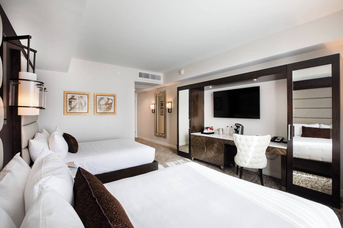 Ein Hotelzimmer mit zwei Betten, einem Schreibtisch, einem Stuhl, einem Spiegel und Bildern an der Wand.