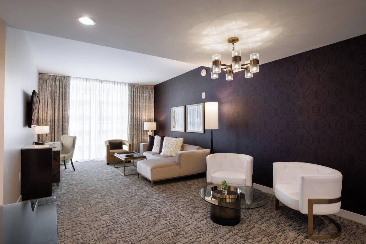 Ein modernes Wohnzimmer mit dunkler Akzentwand, einer Chandelierleuchtre, einem Sofa, einem Couchtisch und einem Fernseher.