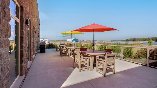 Una terrazza esterna con pareti in pietra, tavoli e sedie in legno e ombrelloni colorati.