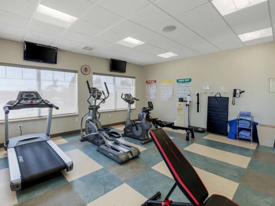 Un gimnasio con cintas de correr, elípticas y una banca.