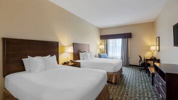 A hotel room with two beds, a desk, a chair, and a television.