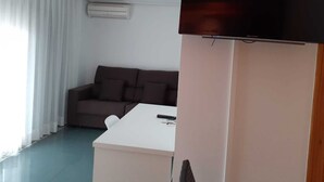 A modern living room with a flat-screen TV mounted on the wall, a white table, and a brown sofa. - Iberflat Hotel Marynton (Benicarlo)