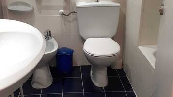 Un baño con inodoro blanco, un bidé, un lavabo y un cubo de basura azul.