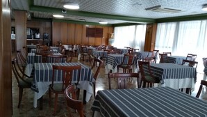 A dining area with multiple tables and chairs, a kitchen in the background, and a patterned ceiling. - Iberflat Hotel Marynton (Benicarlo)