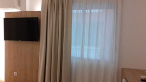 A room with a mounted flat-screen TV, a wooden panel, and a window with sheer curtains. - Iberflat Hotel Marynton (Benicarlo)