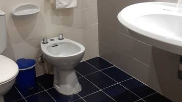 Ein Badezimmer mit Toilette, Bidet, Waschbecken und einer blauen Mülleimer.
