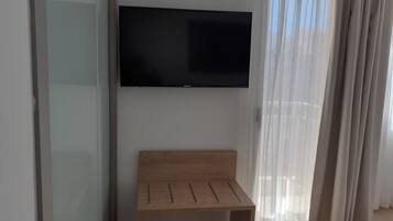Une chambre d’hôtel dotée d’un téléviseur à écran plat fixé au mur, d’un banc en bois et de rideaux en voile.