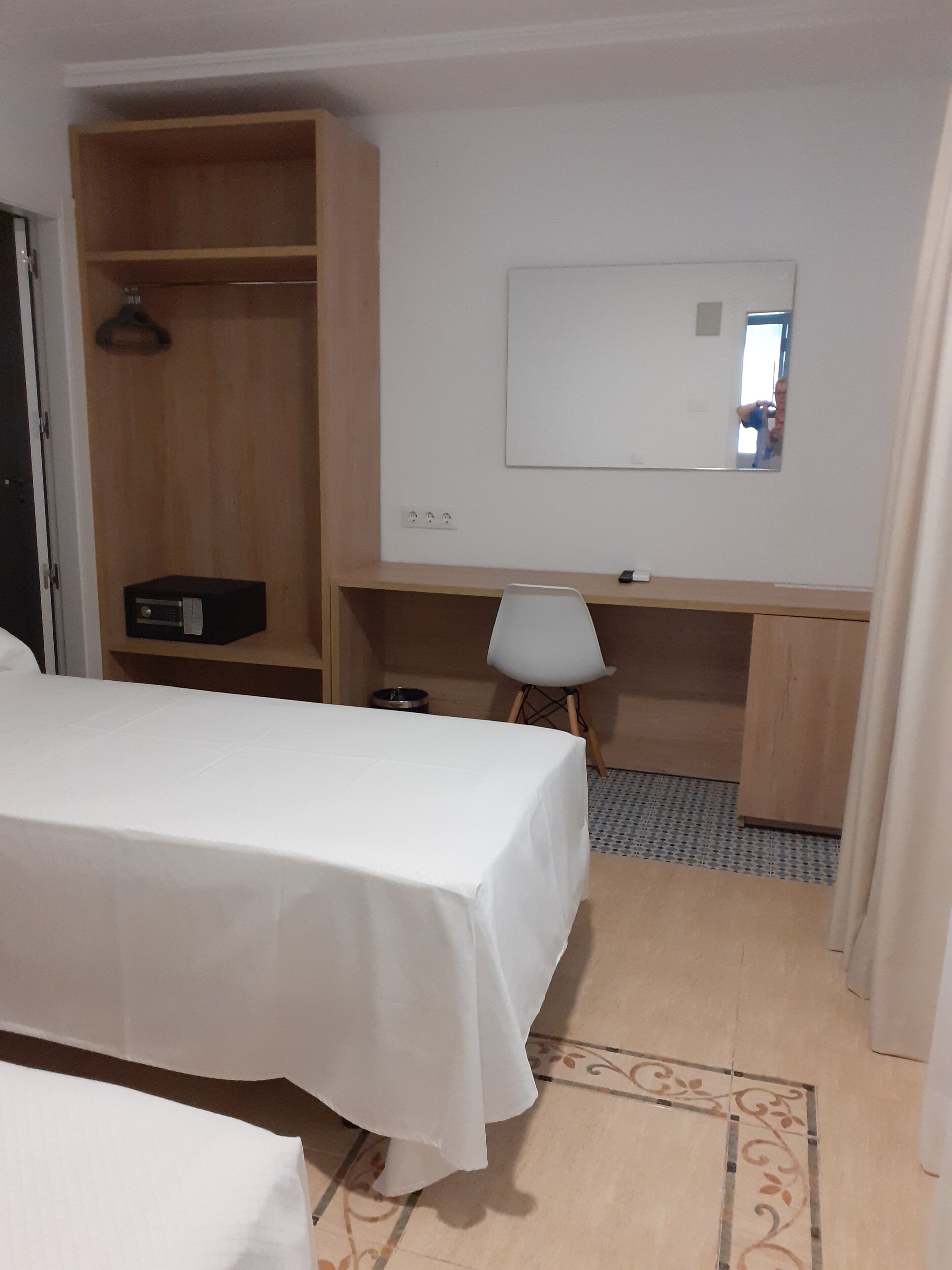 Habitación de hotel con cama, escritorio, silla, armario y espejo.