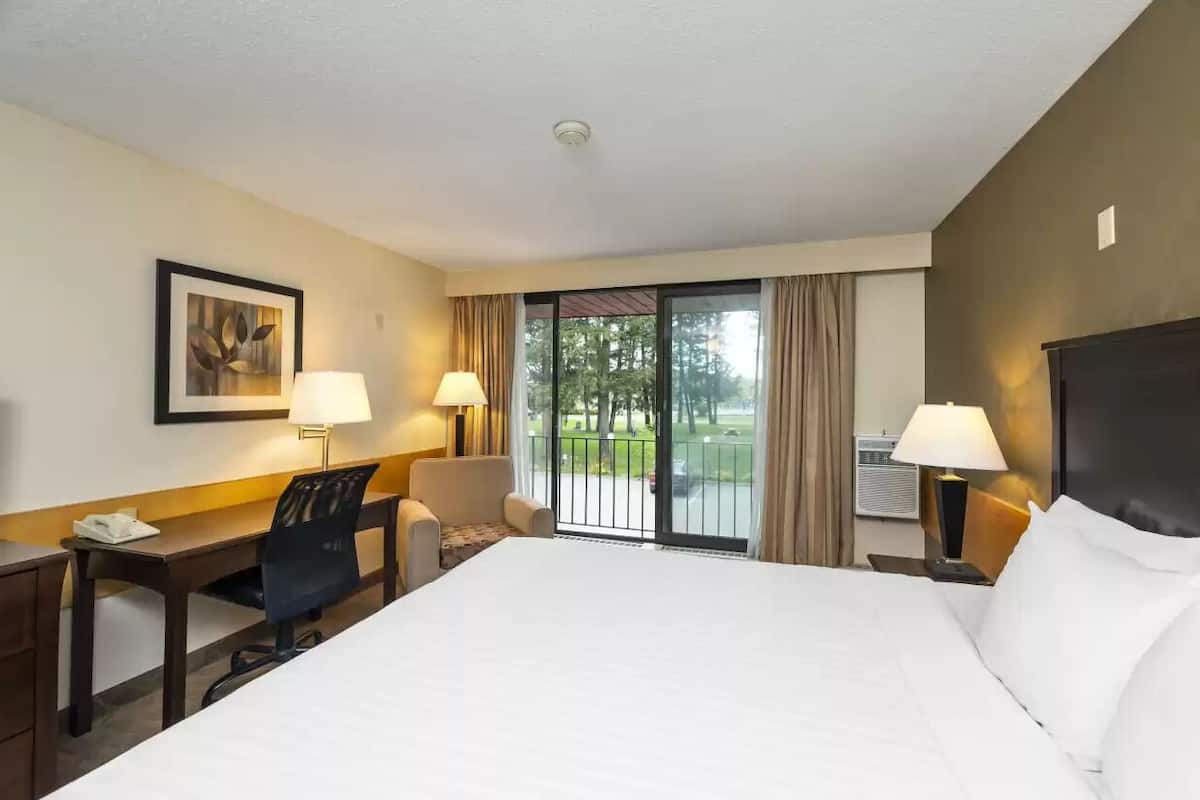 Quarto de hotel com uma cama grande, uma escrivaninha, duas cadeiras, uma janela com vista para uma varanda e um quadro na parede.