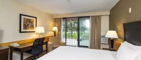 A hotel room with a large bed, a desk, two chairs, a window with a view of a balcony, and a painting on the wall.