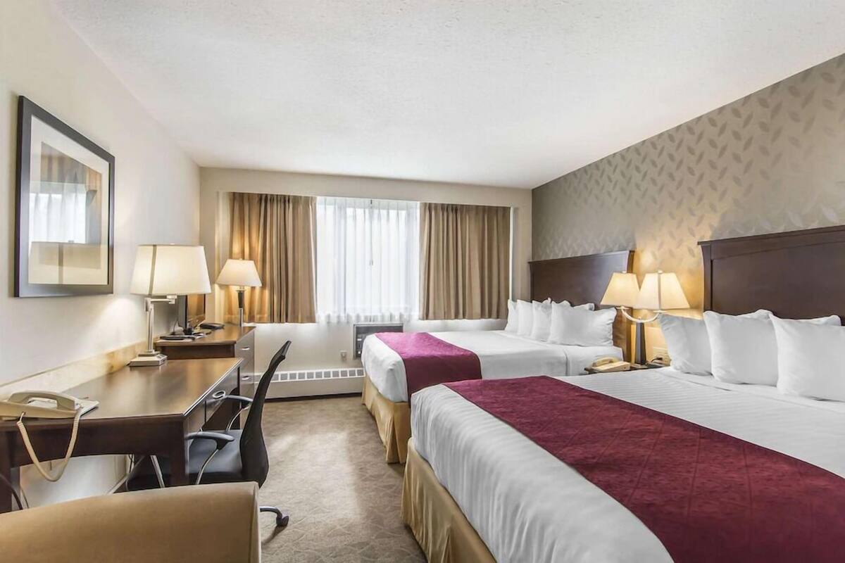 Quarto de hotel com duas camas, uma escrivaninha, uma cadeira e um telefone.