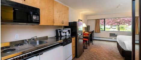 Une chambre d’hôtel compacte comprenant un coin cuisine, un lit, un bureau et une fenêtre donnant sur des arbres en fleurs.