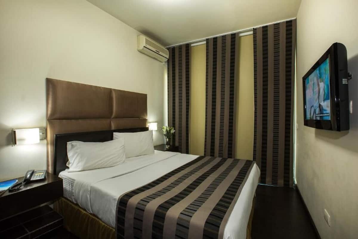 Une chambre d’hôtel avec un grand lit, un téléviseur à écran plat fixé au mur, une table de chevet avec un téléphone et des rideaux à rayures.