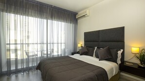 Una camera d'albergo moderna con un letto grande, una testiera, due lampade da comodino, una finestra con tende leggere e vista all'esterno.
