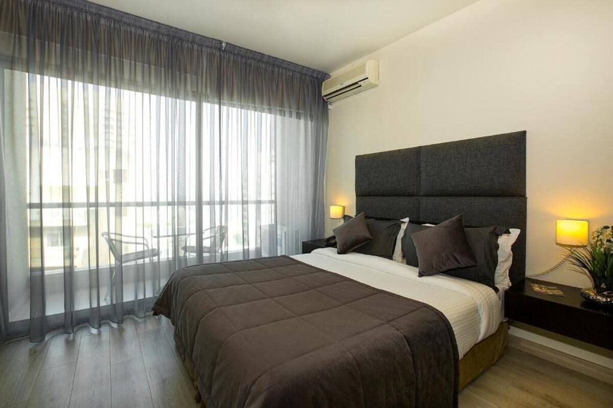 Une chambre d’hôtel avec un lit, une table de chevet, une lampe et une fenêtre avec des rideaux.